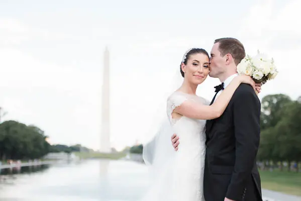 A bride and groom pose for the camera in front of the washington monument.