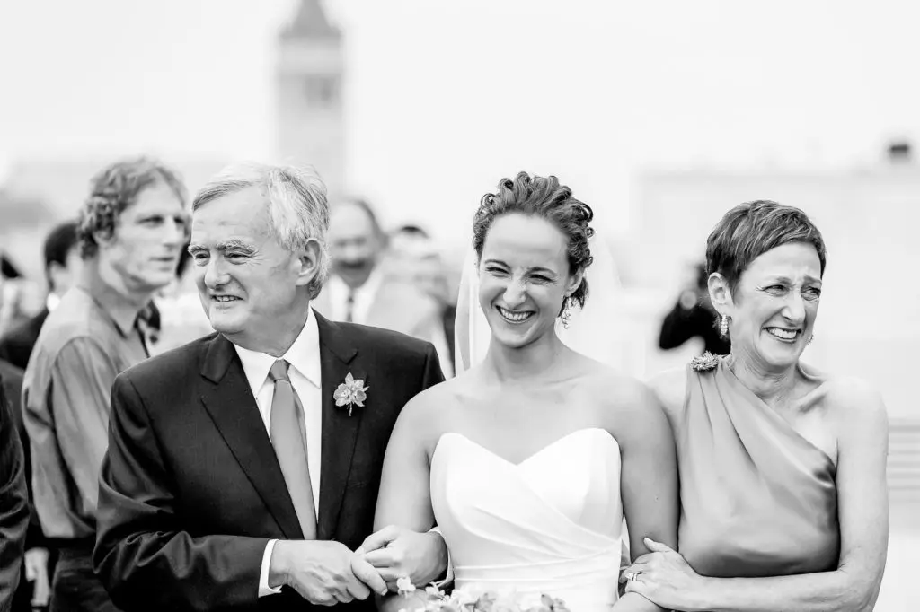 A bride and her parents are smiling for the camera.