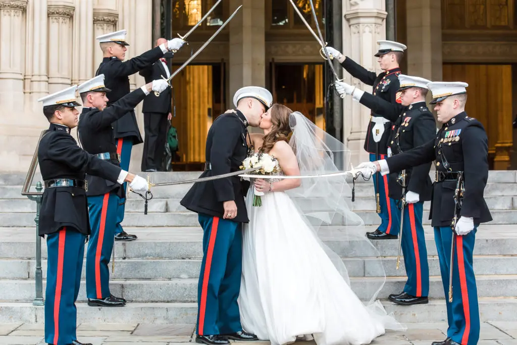 A bride and groom kissing in front of the military.