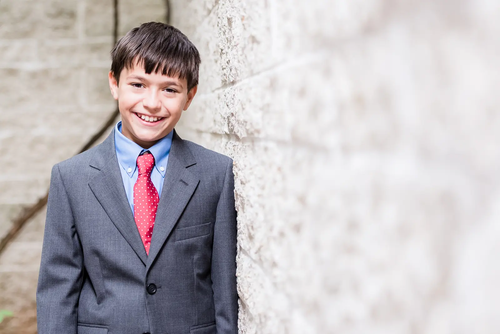 A boy in suit and tie standing next to a wall.