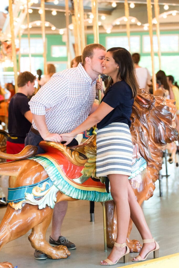 A man and woman kissing on top of a carousel.