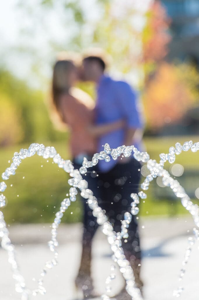 A couple kissing in front of a fountain.