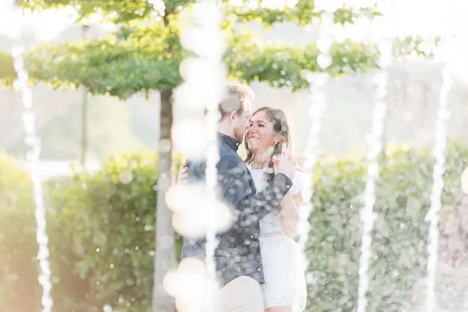 A couple kissing in front of a fountain.