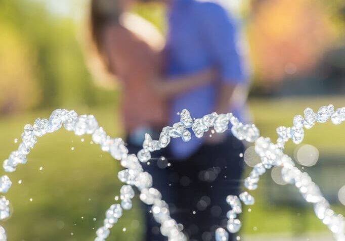 A couple kissing in front of a fountain.